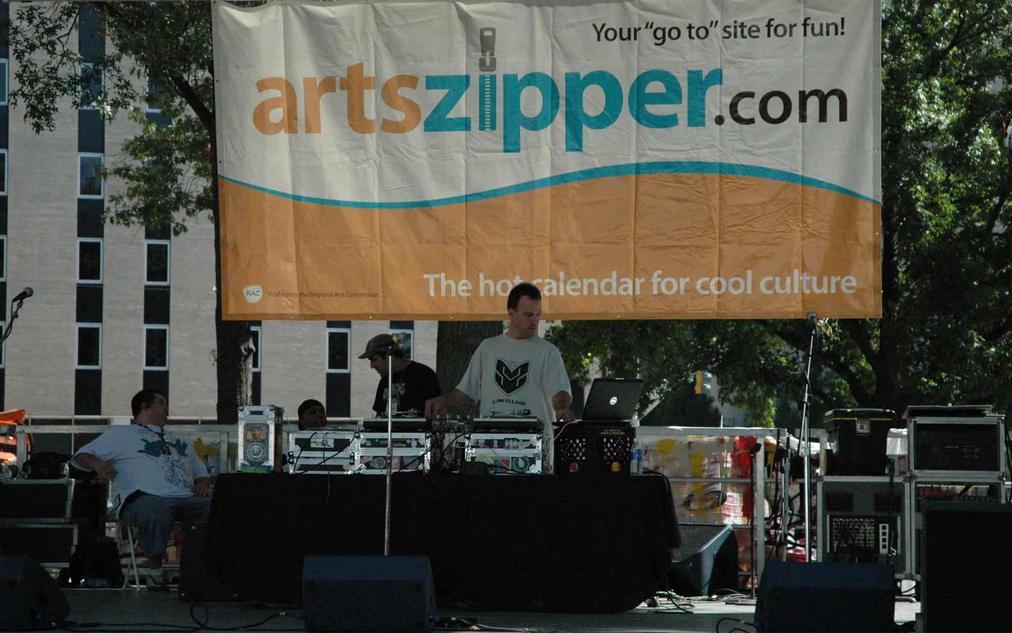 Front View Of Man Djing On Music Stage With A Sign That Says Artzipper.com